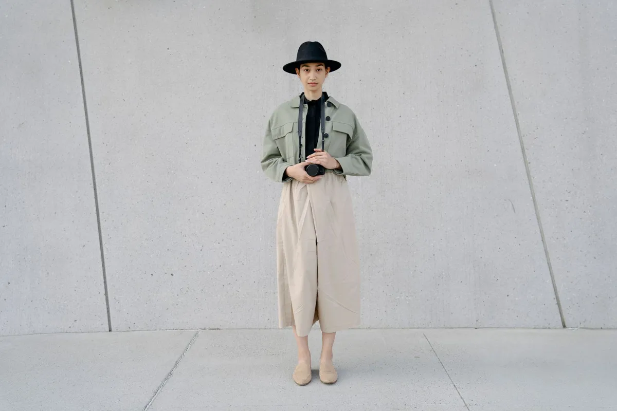 Mode femme minimaliste : veste workwear kaki et jupe-culotte beige ample devant un mur en béton